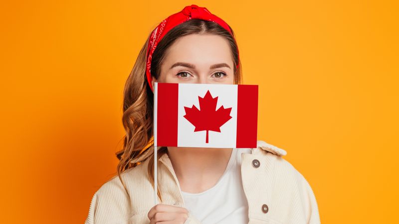 a young woman covers her face with a small flag of canada 1618227837866